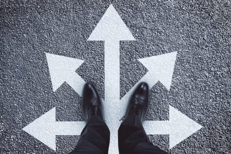 Top view of businessman feet with five arrows in different directions on concrete background. Different direction and leadership concept