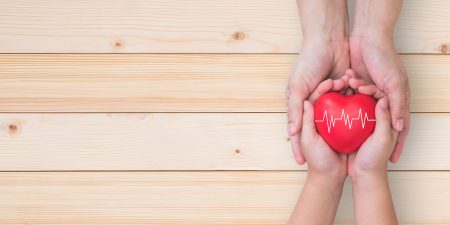 Hands of a child and a grown-up holding a red heart with a white pulse sign