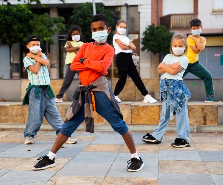 Modern tweens in protective face masks dancing hip-hop on summer street. New urban lifestyle concept during coronavirus. Conscious generation