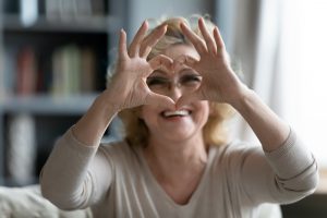 Elderly woman sitting on couch showing heart symbol with fingers