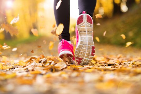 Feet and lower legs of a person wearing pink running shoes running through autumn leaves