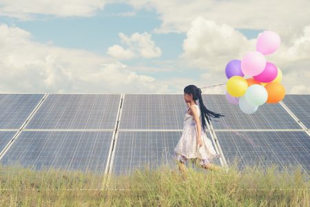 A funny girl carrying colorful balloons running in a meadow with a Solar panel, photovoltaic.