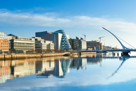 Modern buildings and offices on Liffey river in Dublin on a bright sunny day, bridge on the right is a famous Harp bridge which is named after the author Samuel Beckett