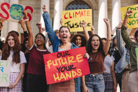 Group of multicultural youth activists shouting slogans and raising their fists during a climate change protest. Vibrant teenagers marching for climate justice and environmental sustainability.