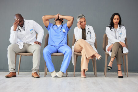 Exhausted, tired and doctors waiting in the hospital with frustration, sad and burnout. Upset, professional and team of healthcare workers sitting in a line in a hallway for meeting in medical clinic.