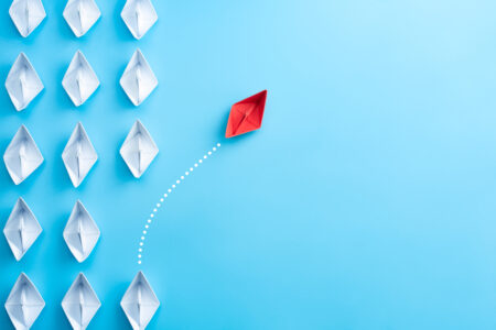 Group of white paper ship in one direction and one red paper ship pointing in different way on blue background. Business for innovative solution concept.