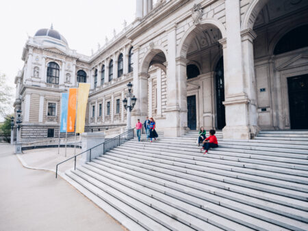 View on the stairways before the main entrance of the University or Vienna. Two female studens sitting on the stairs and three studends, two men and one woman walking downwards.