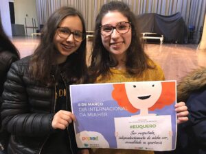 Two teenage girls who participate in the PRESSE programme, showing a poster for the international women's day.